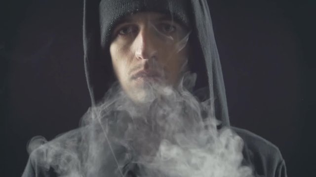 young vaper man exhaling big clouds of smoke with e-cigarette vape in slowmotion