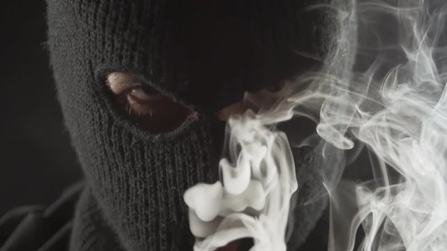 dangerous terrorist in a balaclava smokes e-cigarette vape and makes a lot of smoke.