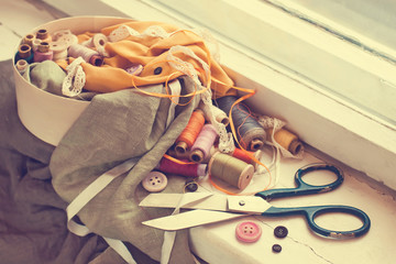 Old scissors, spools of thread, fabric and buttons on the windowsill. Vintage style.