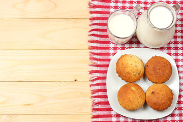 Glass jug pitcher of fresh milk with glass and muffins in a rustic setting on the wood background  with copyspace. Tow view.