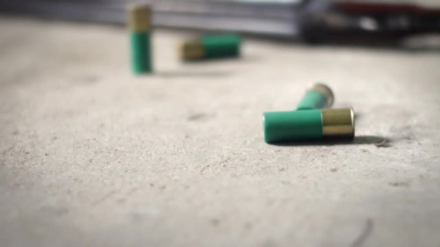 Camera pans by shotgun shells lying on concrete floor near double barrel shotgun
