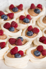Closeup of delicious meringues with fresh organic raspberries and blueberries. Tasty dessert or snack.