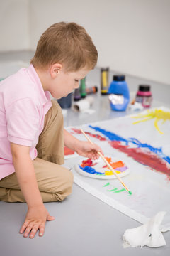 Cute kid boy sitting on the floor and drawing with colorful paints. Child making flag craft. Education, creativity, school activities.