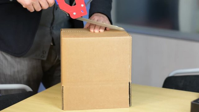 Male hands packing small cardboard box with self-adhesive duct tape in office or warehouse
