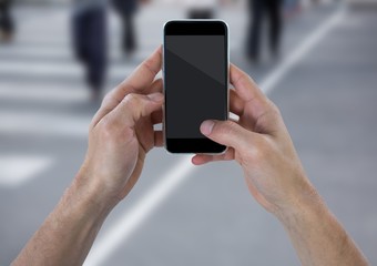 Hands with phone against blurry street with people