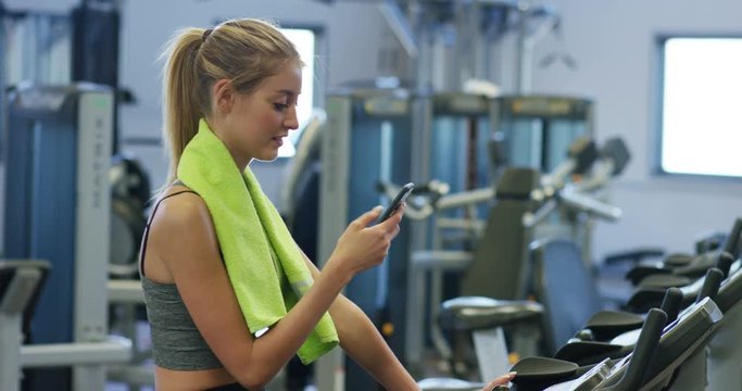 Young beautiful girl in a gym, shakes her legs on a cycling simulator, with a phone in her hand. The concept: to love sports, to attend a gym, proper nutrition, a slender body, to be healthy.