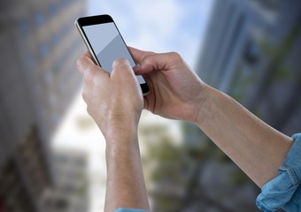 Hands with phone against blurry buildings