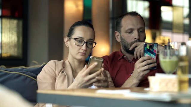 Young couple staring at smartphone and drinking in cafe
