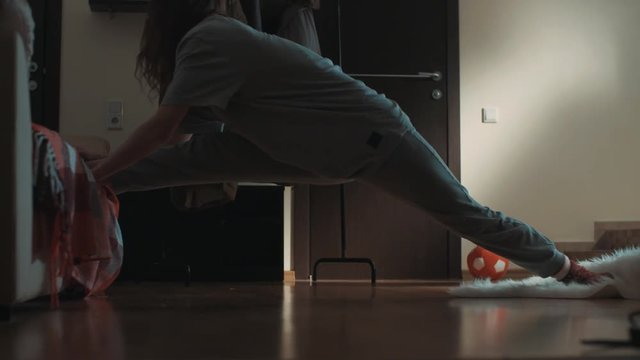 Young flexible brunette caucasian woman in living room standing one foot on couch, slips on carpet and accidentally makes splits, stretches across floor, slow motion