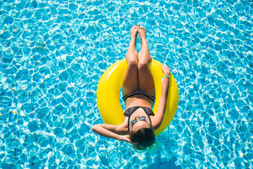 Happy young woman in bikini with rubber inflatable float, playing and having a good time at water pool on a summer hot day