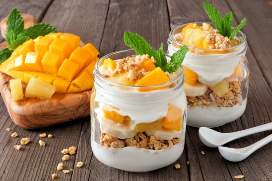 Mango and pineapple parfaits in mason jars, scene on a rustic wood background