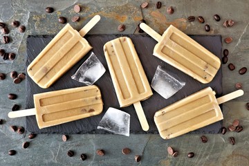 Coffee and chocolate popsicles on a slate server, overhead view over a stone background