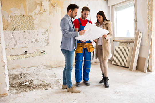 Young couple looking blueprints of their home with handyman