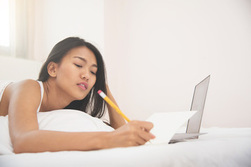 Asian woman writing with pencil on her bed. copy space.