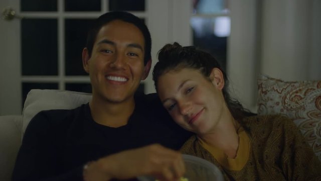 A young couple watching television and eating popcorn together, kiss on the cheek