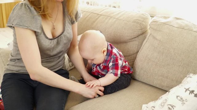 Young mother puts the socks on to her 6 months baby boy on the sofa