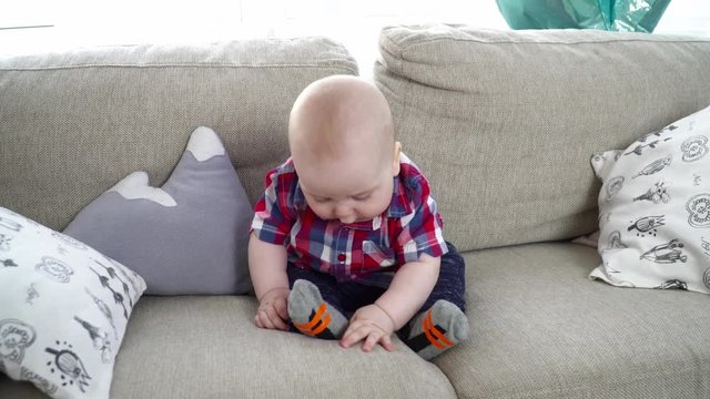 Small cute baby boy sitting and looking around on the sofa
