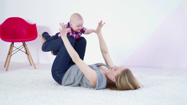 Young mother swinging her small baby son on her legs