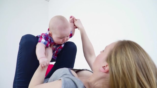 Young mother swinging her small baby son on her legs closeup