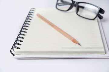 Blank  notebook with a Pencil and eyeglasses on white blackground, suit for writing and thinking concept.