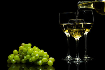 Glasses for wine and a bunch of grapes on a black background