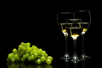 Glasses for wine and a bunch of grapes on a black background