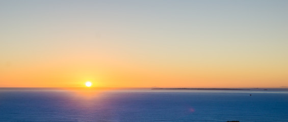 Abstract effect defocused background image Orange glow of sunrise sitting on horizon over blue sea panorama.