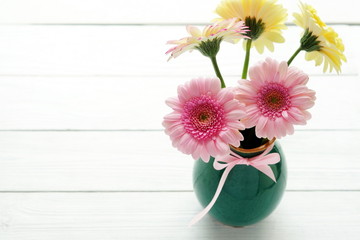 Bouquet of pink and cream gerberas in a green vase on a white wooden background
