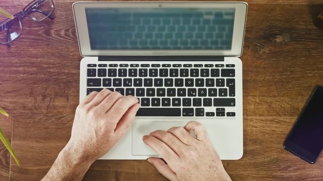 Man's hands typing on laptop keyboard on a wooden desck