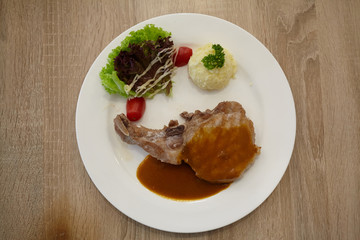 Pork chops steaak grilled with black pepper sauce and salad on white plate.