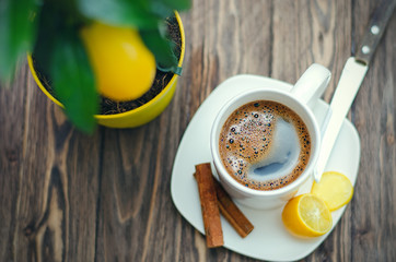 Coffee in white cup on wooden table opposite a defocused background with lemon tree.