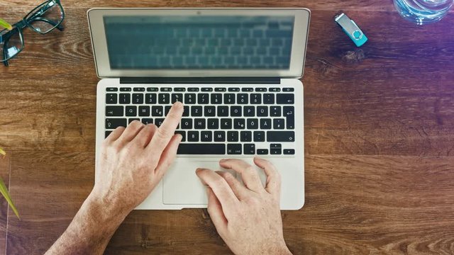 Man's hands typing on laptop keyboard on a wooden desck