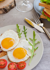 Breakfast table with fried eggs, bacon, cherry tomatoes, sanwiches