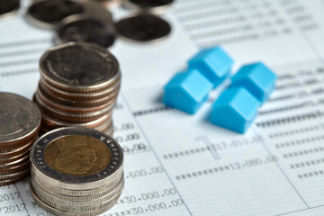 Coins stack with blue home toys on passbook. Saving, income and home loan concept.