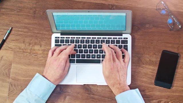 Man's hands typing on laptop keyboard on a wooden desck