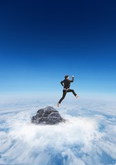 Business man jumping off mountain peak in the clouds