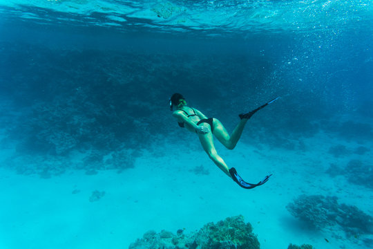 Underwater photo of woman snorkeling and free diving in a clear tropical water at coral reef