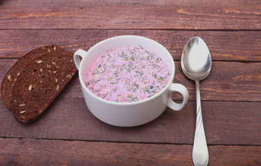 Popular spring cold soup okroshka with yoghurt. Okroshka in a bowl and slices bread on wooden table. Selective focus