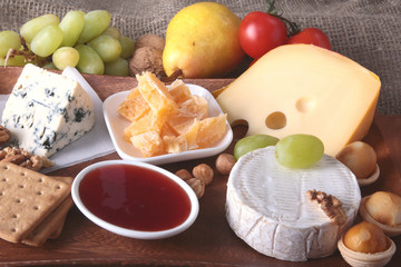 Assortment of cheese with fruits, grapes and nuts on a wooden serving tray.
