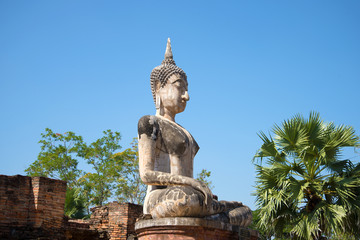 A view of the ancient sculpture of a sitting Buddha on the ruins of the Buddhist temple of Wat Mae Chon on a sunny afternoon. Sukhothai, Thailand