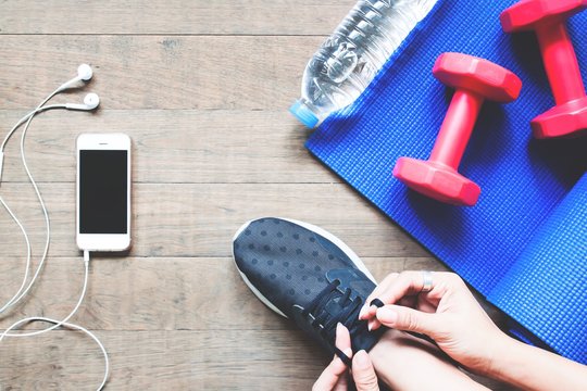 Overhead View Of Woman In Black Sneaker With Smartphone And Sport Equipment On Wood Floor