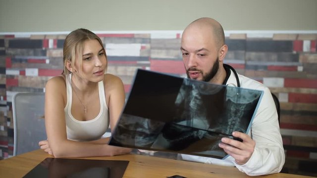 bald adult 30s doctor is showing x-rays to a patient and discuss it