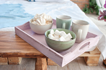 A pink breakfast tray on which lie cups for tea and for coffee, white marshmallows are in the plates