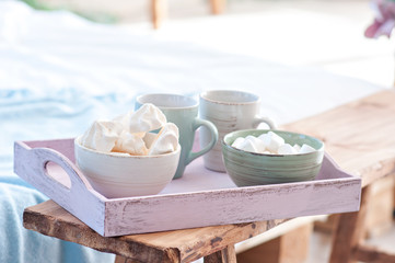 A pink breakfast tray on which lie cups for tea and for coffee, white marshmallows are in the plates