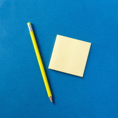 Neon yellow pencil and notepad on blue background