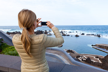 Kobieta blondynka fotografująca smartfonem brzeg oceanu.