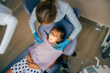 Female dentist with mirror checking patient girl teeth up at dental clinic office