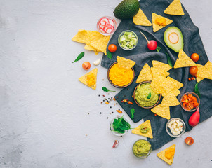 A delicious Bowl of Guacamole next to fresh ingredients on a table with tortilla chips and salsa. Flat lay. Copy space