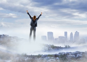 Fototapeta na wymiar Business woman cheering on misty mountain peak against skyline