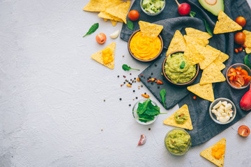 A delicious Bowl of Guacamole next to fresh ingredients on a table with tortilla chips and salsa